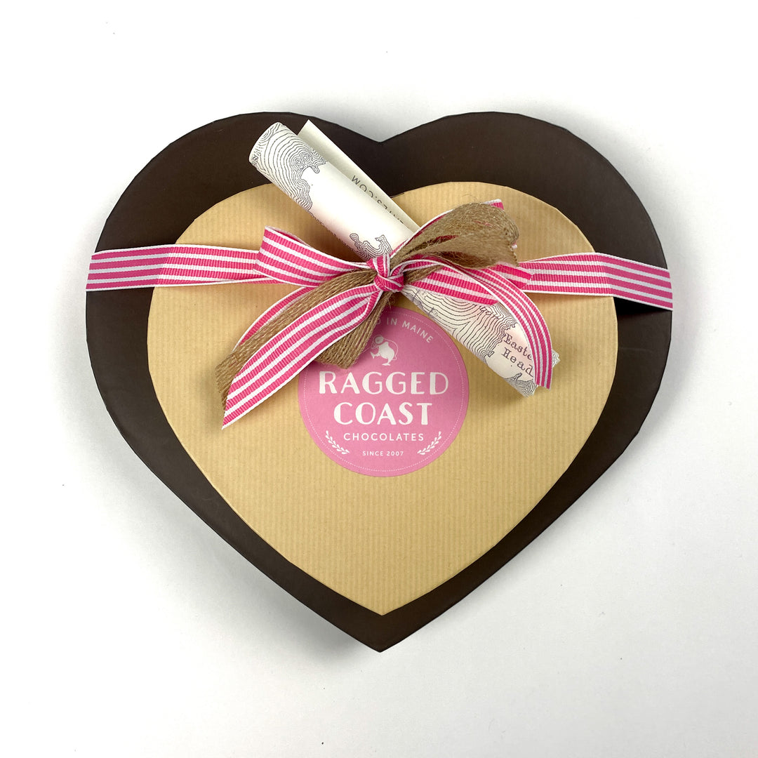 Ragged Coast Chocolates' "Two Hearts - 50 Pieces" box, shaped like a heart and trimmed with a pink ribbon and scroll, unveils its indulgent collection of chocolate truffles and sea salt caramels.