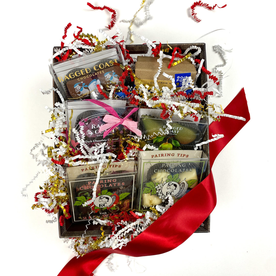 The Valentine's Day Variety Gift Pack by Ragged Coast Chocolates features assorted chocolate truffles in transparent packaging. Decorated with festive shredded paper and topped with a red ribbon, this gift box is perfect for any occasion.