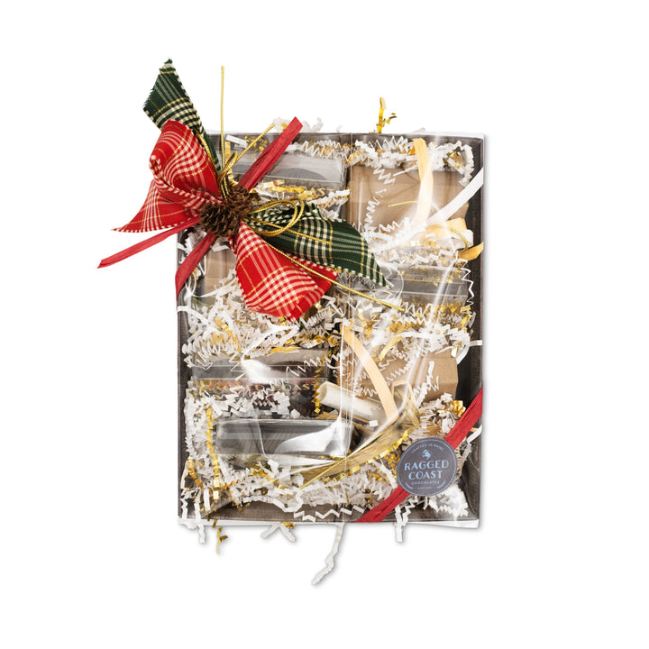 The Chocolate Sampler Gift Box for the Holidays by Ragged Coast Chocolates features a festive design with red and green plaid ribbons and a pine cone. It contains shredded paper, with glimpses of luxurious chocolate truffles, and proudly displays the "Ragged Coast" label.