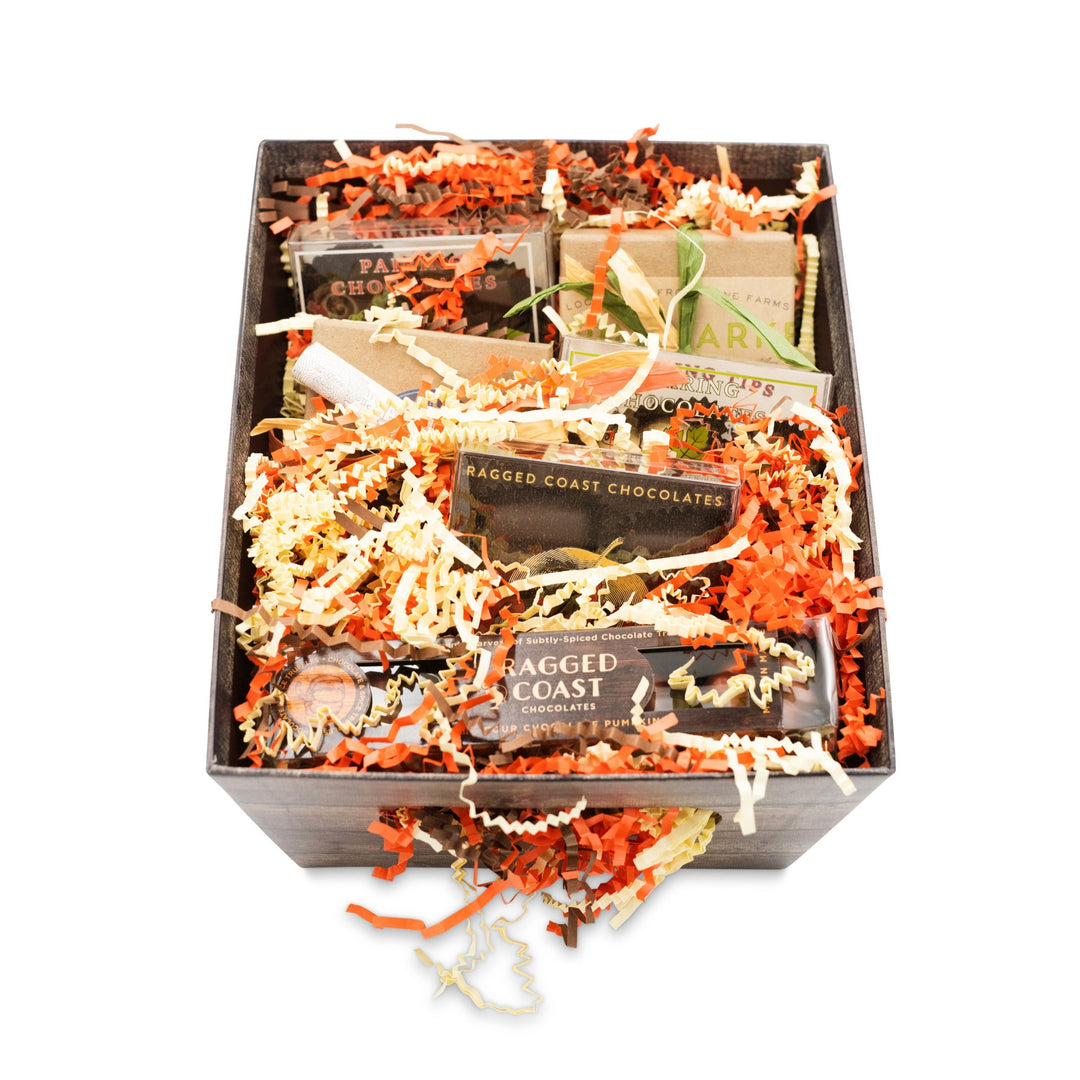 The Ragged Coast Chocolates Autumn Chocolate Sampler Gift Box, brimming with an assortment of chocolate bars, nestled neatly among orange and white crinkle paper.