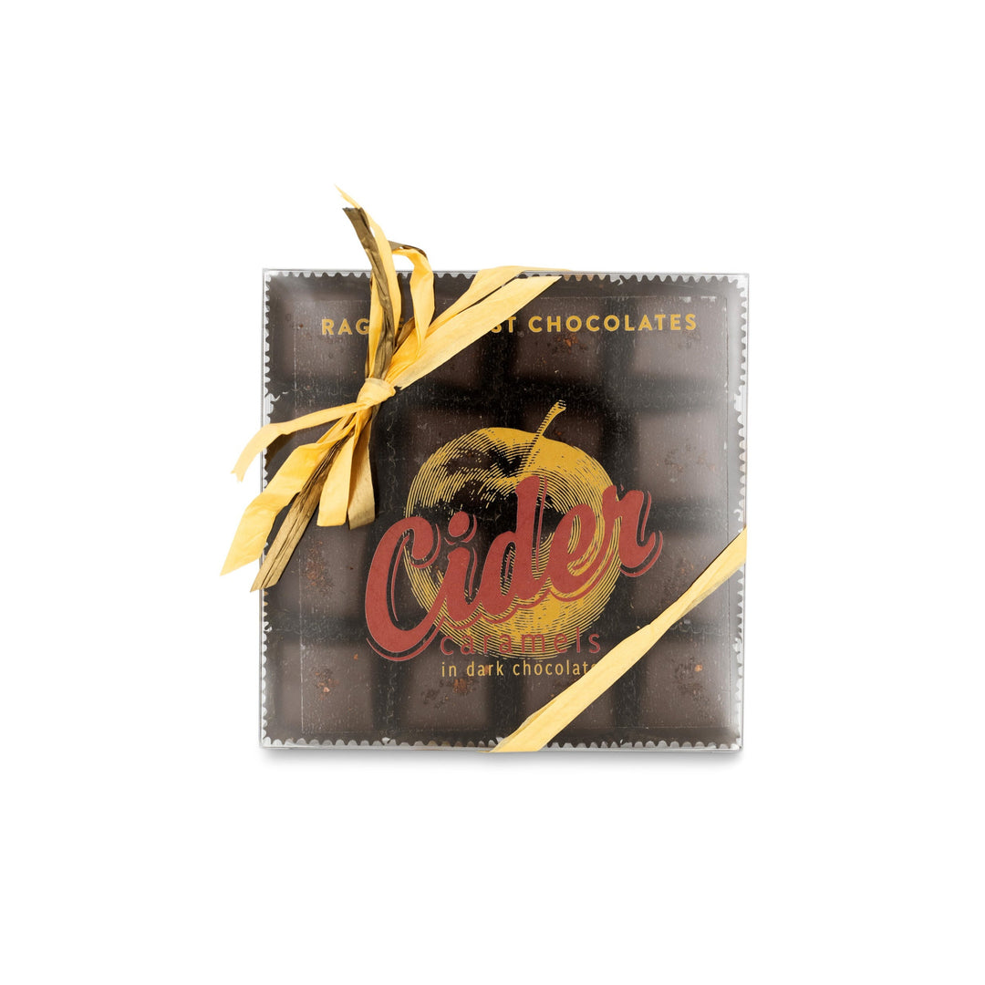 A box of New England Cider Caramels in Bittersweet Chocolate, wrapped with a yellow ribbon. The box features an apple illustration and text that reads "Ragged Coast Chocolates".