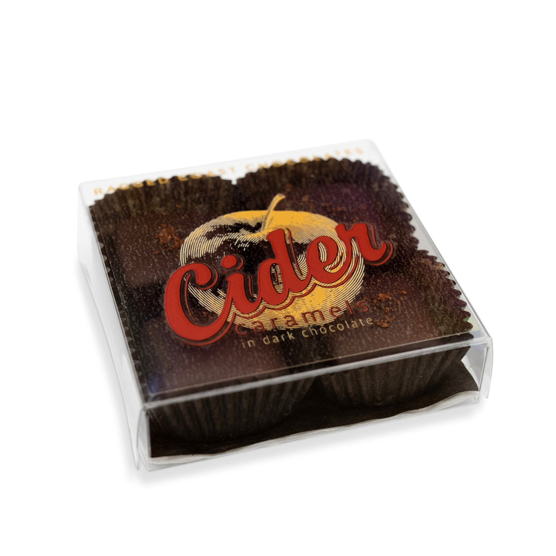 A clear plastic package containing Ragged Coast Chocolates' New England Cider Caramels in Bittersweet Chocolate, with a label featuring an apple and the text "Cider Caramels" in bold red letters. The apple-spiked spiced caramel paired with bittersweet chocolate creates an irresistible treat.