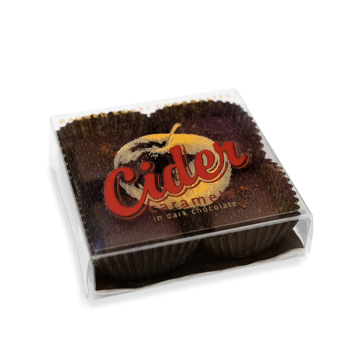 A clear plastic package containing Ragged Coast Chocolates' New England Cider Caramels in Bittersweet Chocolate, with a label featuring an apple and the text "Cider Caramels" in bold red letters. The apple-spiked spiced caramel paired with bittersweet chocolate creates an irresistible treat.