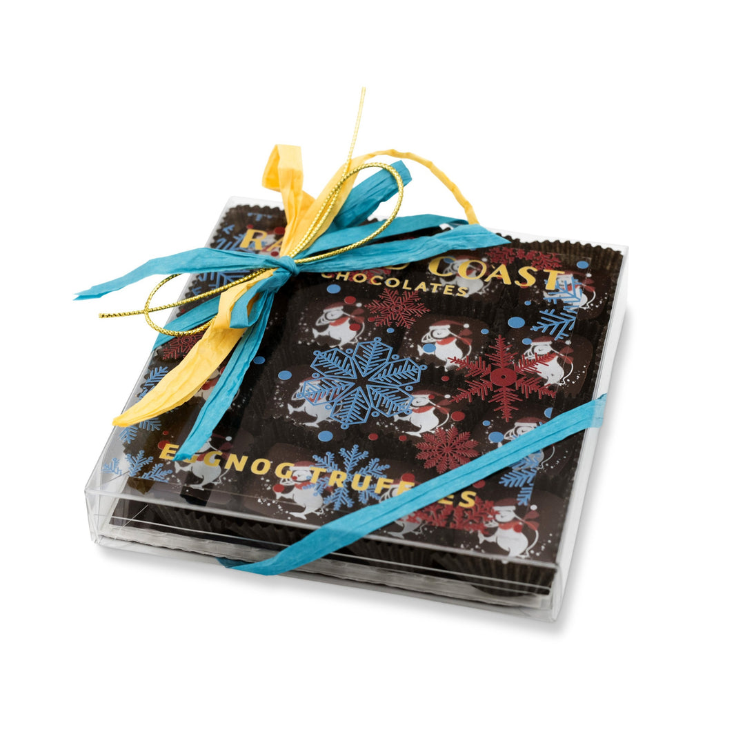 A box of Ragged Coast Chocolates, adorned with blue and yellow ribbons and showcasing snowflake and snowman designs, includes delightful Eggnog and Bittersweet Chocolate Truffles that are perfect for holiday enjoyment.