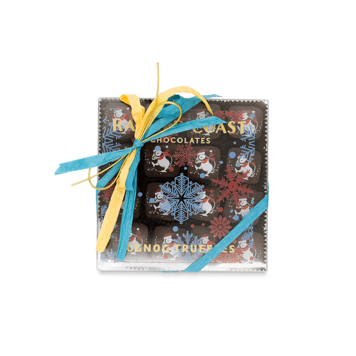 A square box of Eggnog and Bittersweet Chocolate Truffles by Ragged Coast Chocolates, adorned with blue and yellow ribbons, showcases snowman illustrations and a snowflake design. Inside, enjoy treats like creamy ganache centers and white chocolate truffles ideal for a holiday celebration.