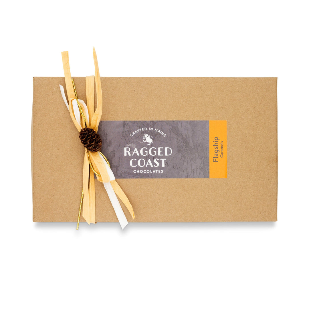 A brown gift box featuring the "Ragged Coast Chocolates" logo and a "Flagship Sea Salt Caramels" label, elegantly adorned with twine and a pinecone. Inside, indulge in the luxurious blend of Ecuadorian dark chocolate enhanced with a hint of Maine sea salt.