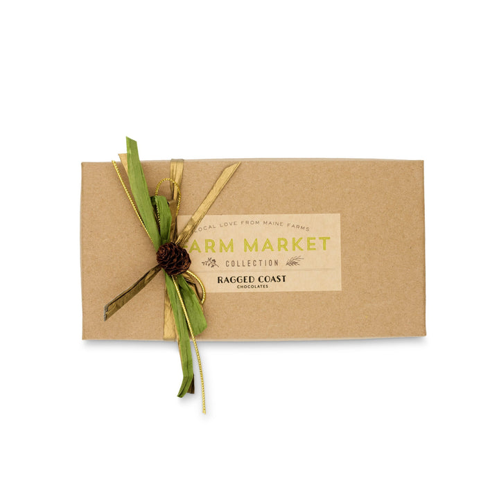 A brown gift box labeled "Maine Farm Market Truffle Collection" from Ragged Coast Chocolates is elegantly tied with a green and gold ribbon, featuring a small pinecone decoration. Inside awaits the delight of exquisite dark chocolate truffles made with Maine farm products.