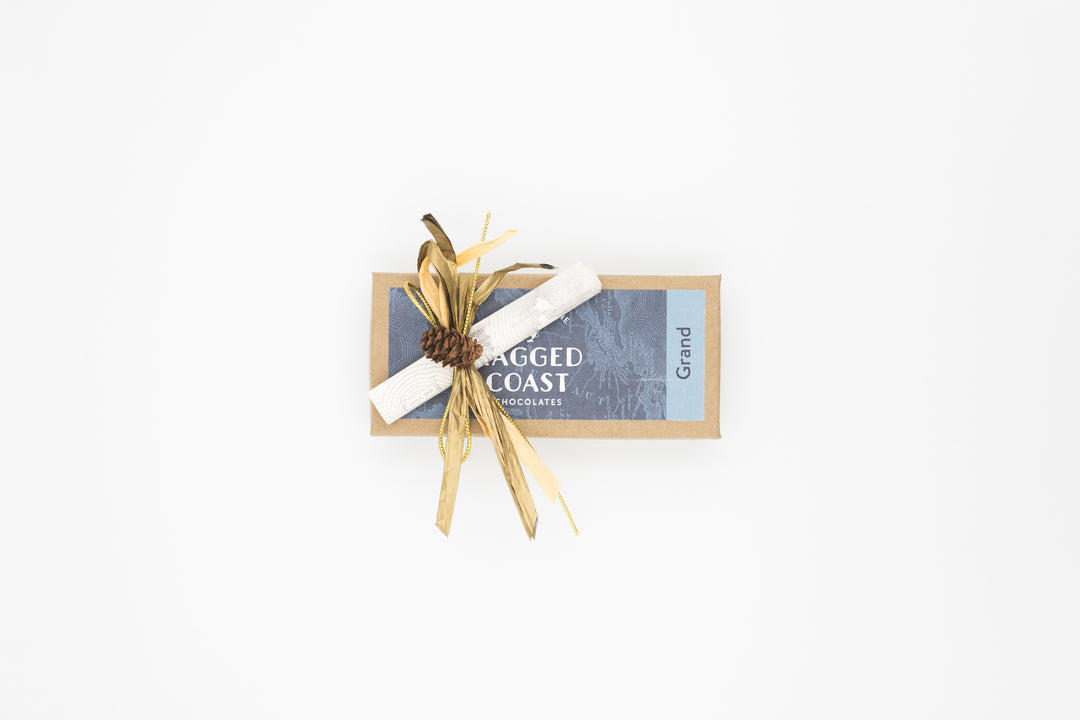 Adorned with a decorative bow crafted from paper and wheat stalks, a rectangular box from "Ragged Coast Chocolates" holds the delightful Eight-Piece Chocolate Party Favor or Thank You Gift, featuring an assortment of milk and dark chocolate truffles.