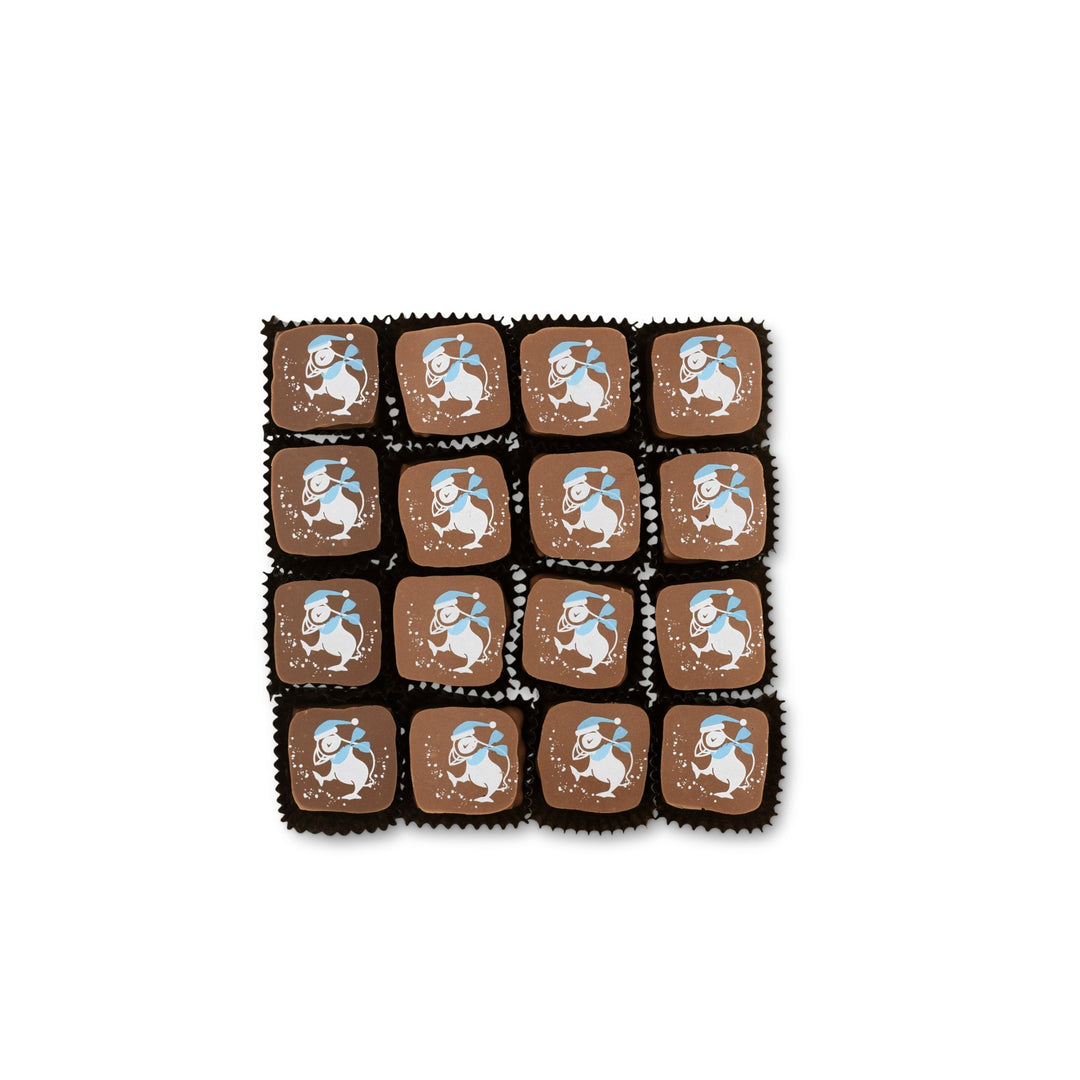 The Ragged Coast Chocolates' "Hot Chocolates" for the Holidays features a grid of 16 brown chocolate squares, each adorned with a white and blue cartoon lamb design, which delicately conceals a creamy chocolate ganache inside.