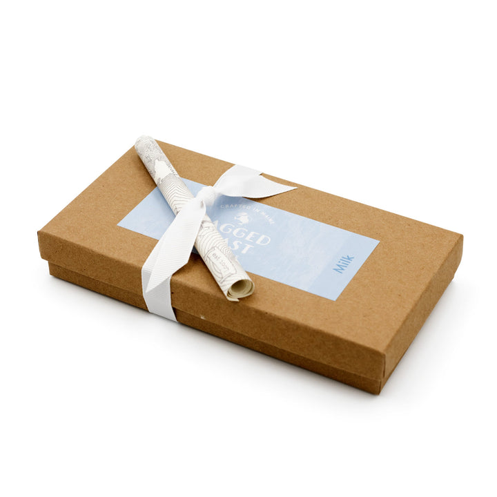 A brown recyclable paperboard box from Ragged Coast Chocolates, marked with a blue label and tied with a white grosgrain ribbon, holds the Milk Chocolate Truffle Assortment. A rolled scroll elegantly sits atop, promising delightful treats inside.