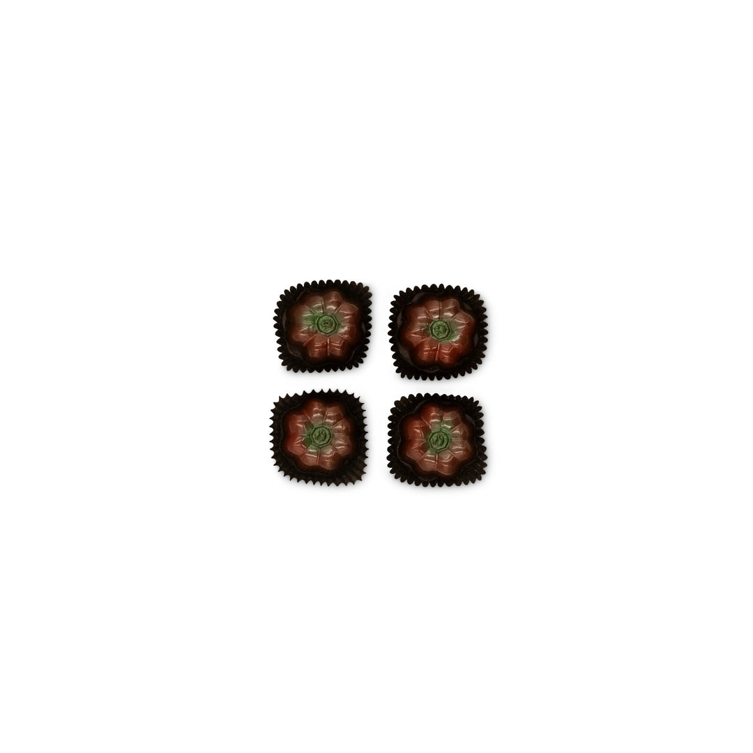 Four flower-shaped Pumpkin Patch Chocolate Truffles from Ragged Coast Chocolates with green centers in brown wrappers arranged in a square on a white background – a delightful seasonal treat.