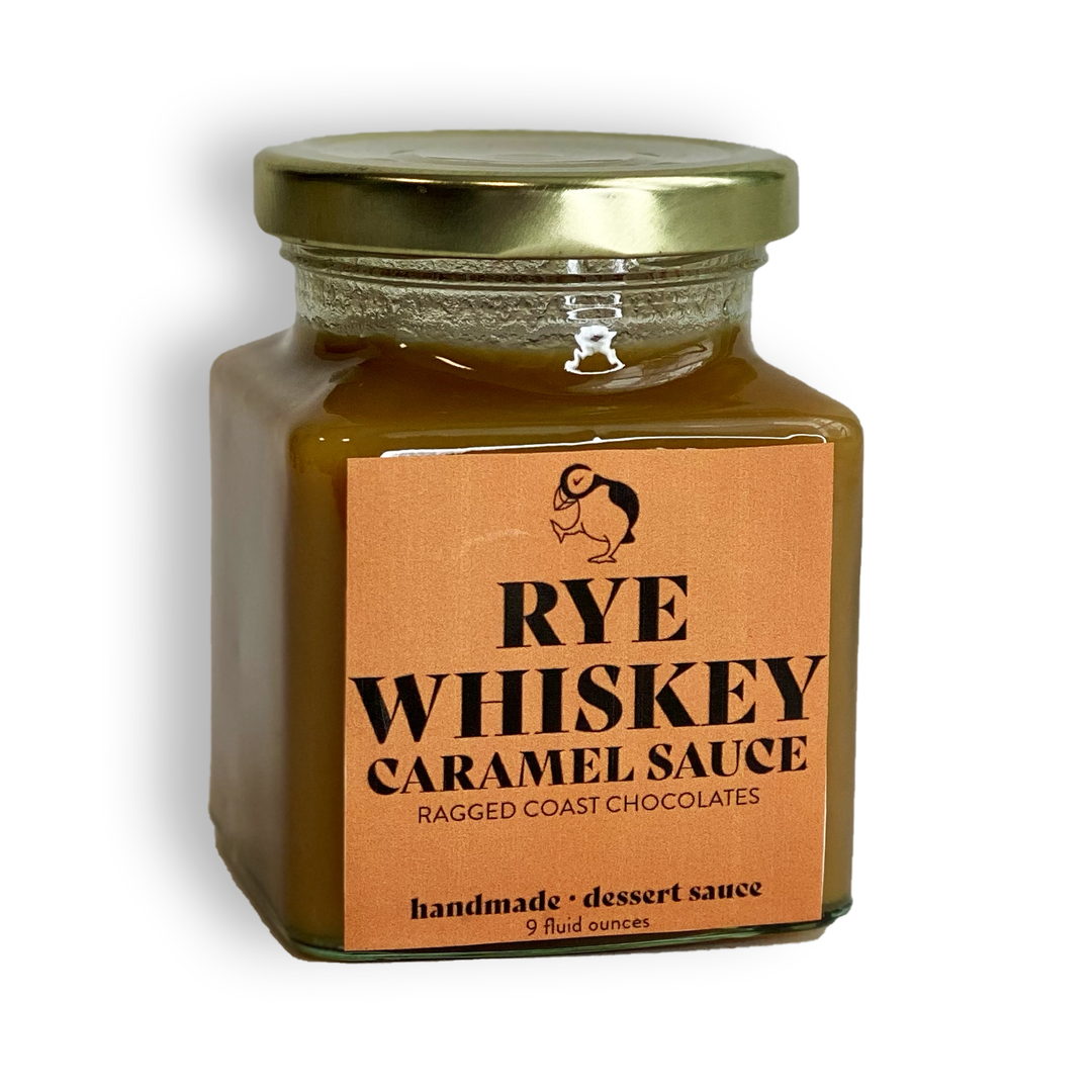 A 9-fluid-ounce glass jar of Rye Whiskey Caramel Sauce from Ragged Coast Chocolates, made with organic sugar and labeled as a handmade dessert sauce—perfect drizzled over peanut butter ice cream.