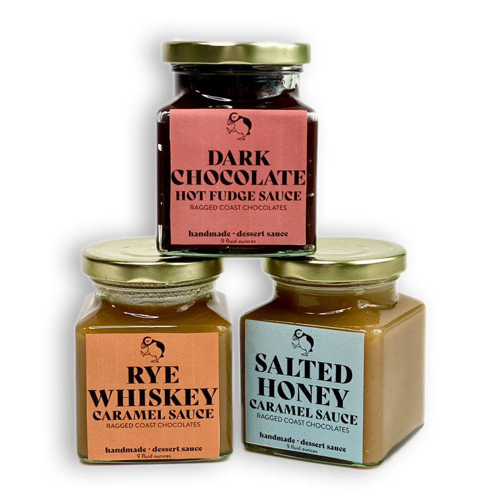 Three jars of handmade dessert sauces from Ragged Coast Chocolates: Dark Chocolate Hot Fudge Sauce, Rye Whiskey Caramel Sauce, and Salted Honey Caramel Sauce.