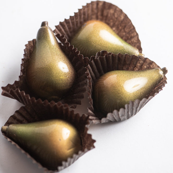 Four delectable Pear Champagne Truffles for the Holidays by Ragged Coast Chocolates, crafted from bittersweet chocolate with a shiny, metallic gold and green surface, each nestled in a brown paper cup.