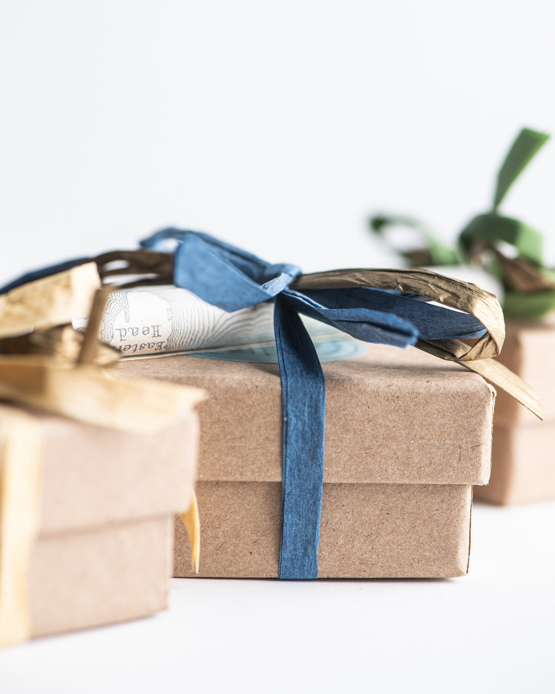 Close-up of small, kraft paper gift boxes, each adorned with colorful ribbon bows in shades of blue and gold, adding a festive touch perfect for gifting the Pocket Chocolate Collection for the Holidays by Ragged Coast Chocolates.