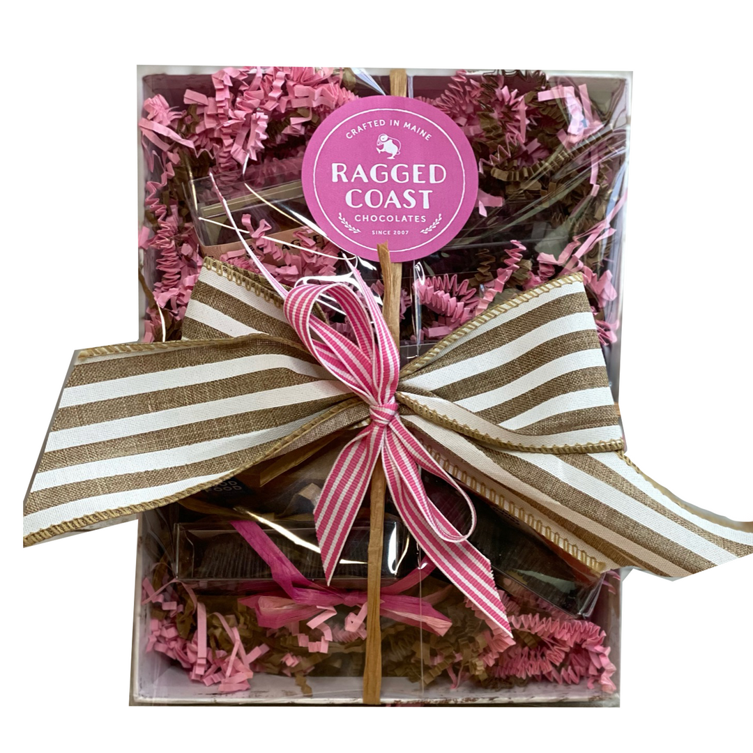 Ragged Coast Chocolates' Valentine's Day Variety Gift Pack, adorned with a large brown and white striped bow and featuring pink crinkle paper inside.